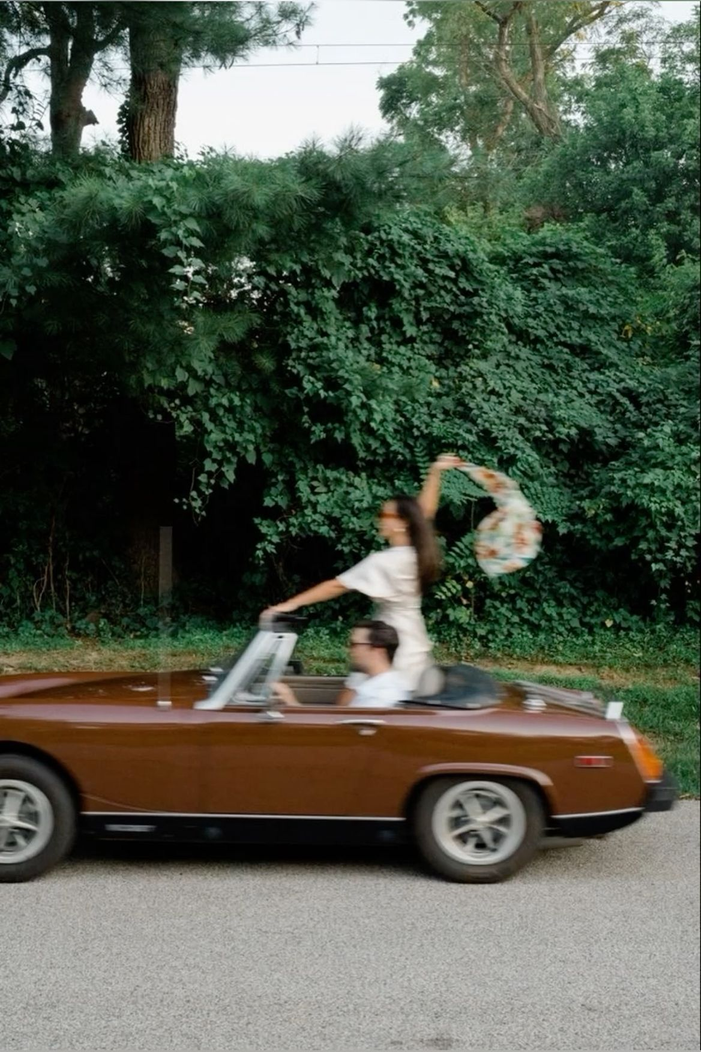 A classic convertible moving through a leafy street
